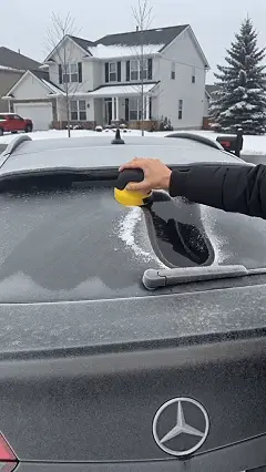 Cordless electric snow scraper clearing frost from vehicle glass