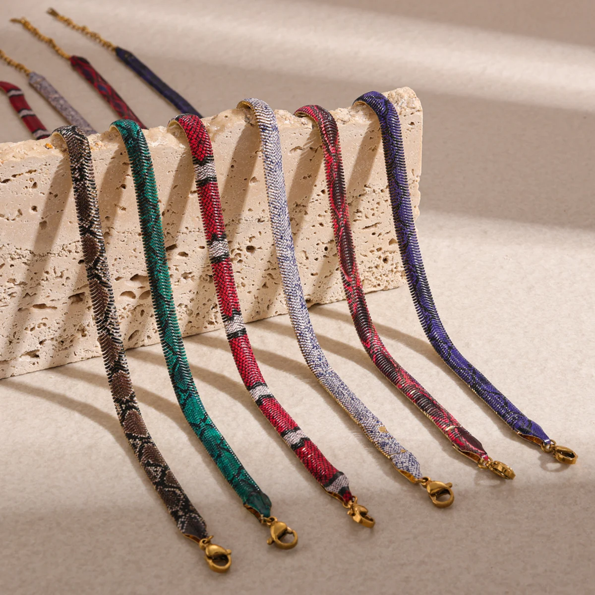 Six serpent necklaces in different colourways lined up on stone