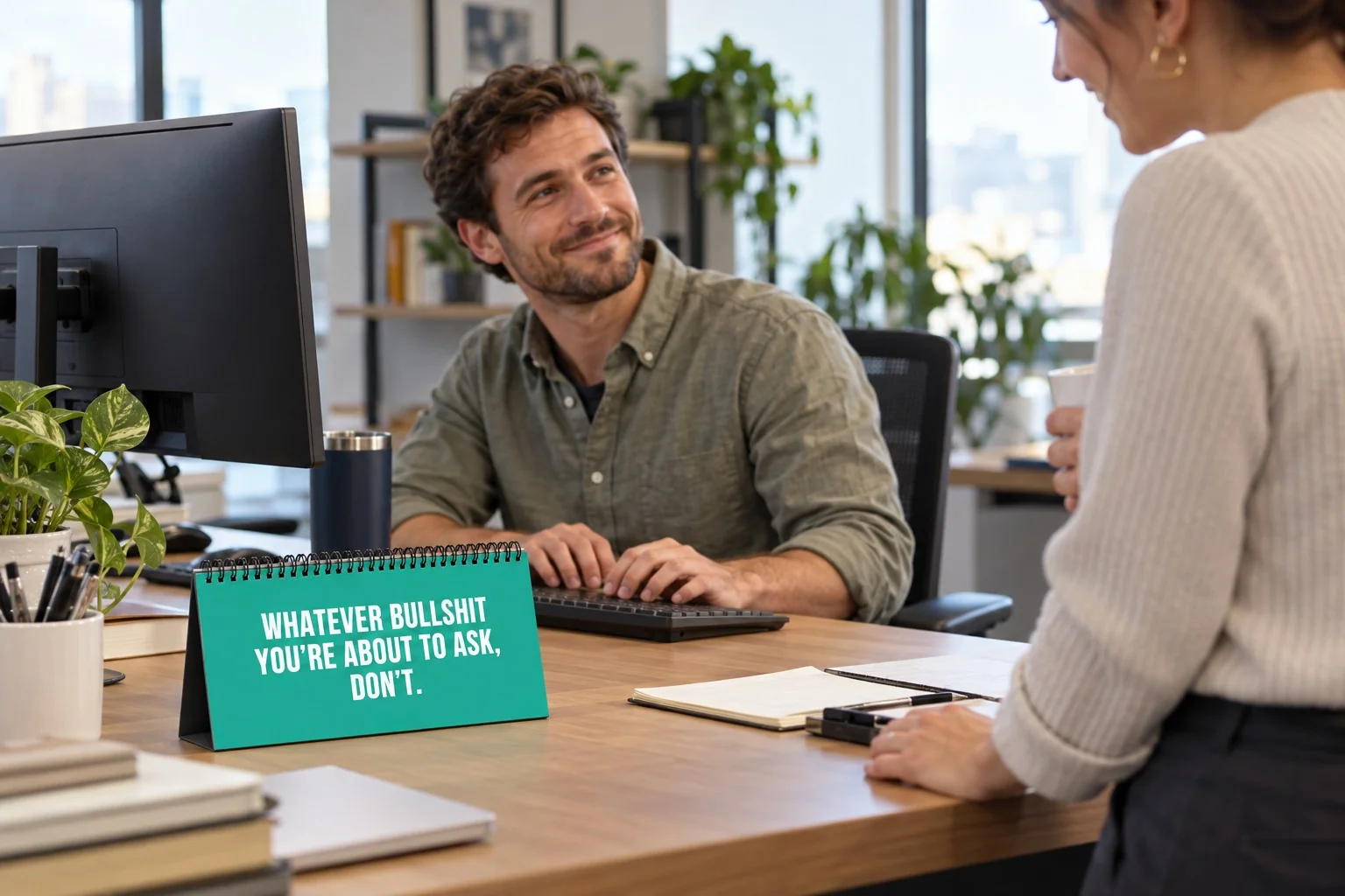 A turquoise desk sign displaying its bold white sarcastic message beside an office worker's keyboard