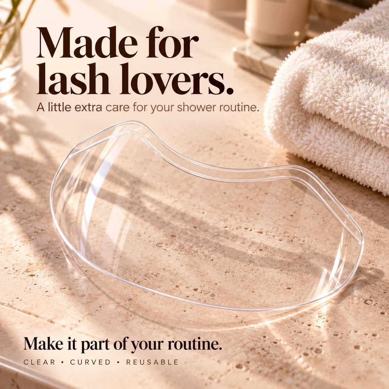Transparent lash shower shield on a warm beige bathroom vanity beside soft towels